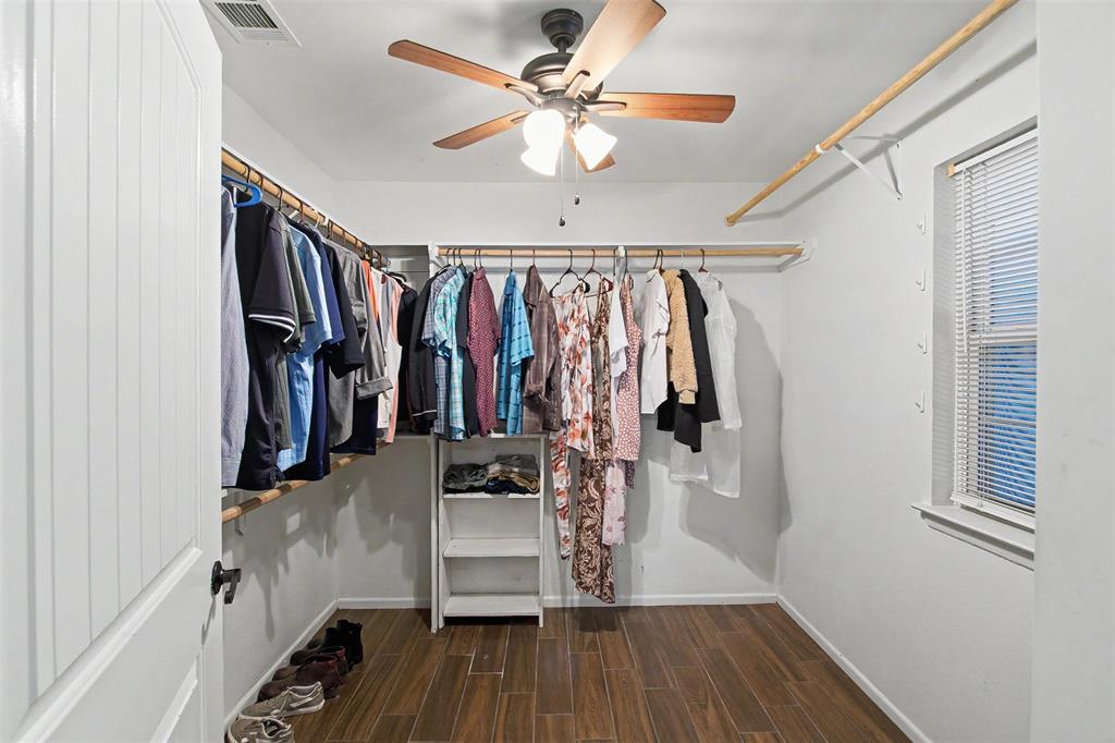 Walk-in closet featuring wood-finish flooring, built-in shelving, multi-level hanging rods, and a ceiling-mounted light fixture with a fan