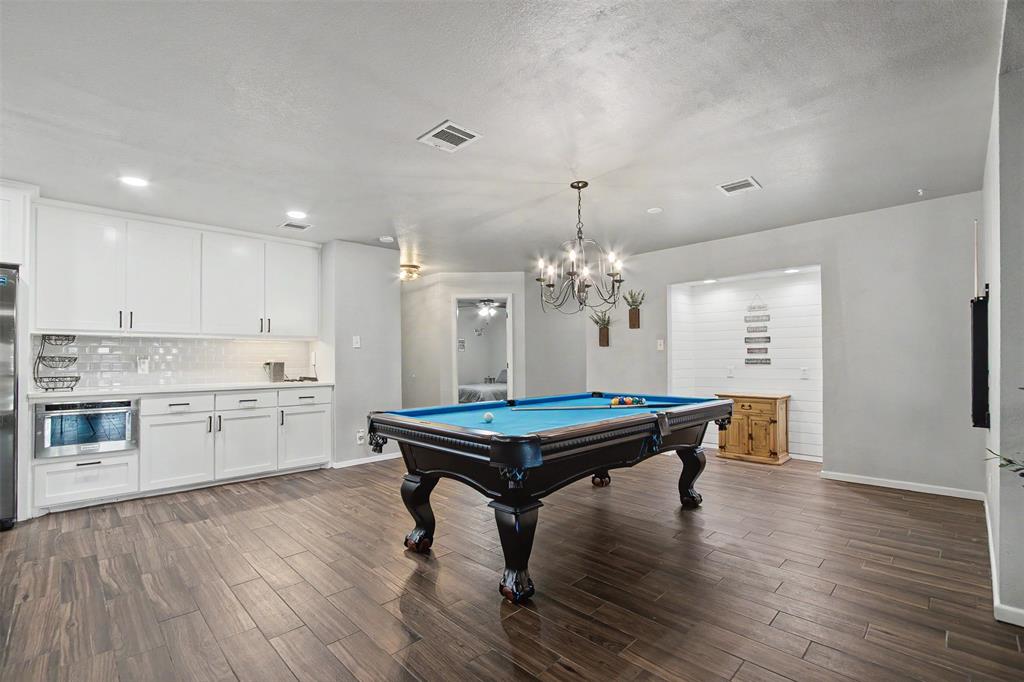White shaker-style cabinetry with integrated microwave, wood-finish flooring, recessed lighting, and a multi-arm chandelier