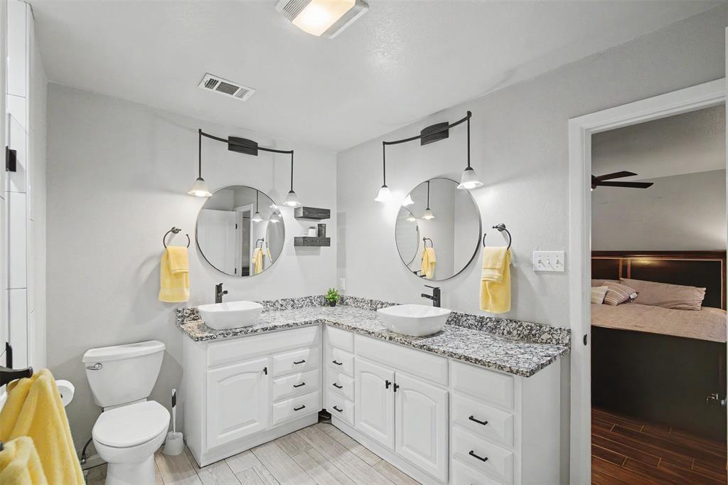 Dual vanity featuring white cabinetry, stone-patterned countertops, two round mirrors, and black-finish hardware