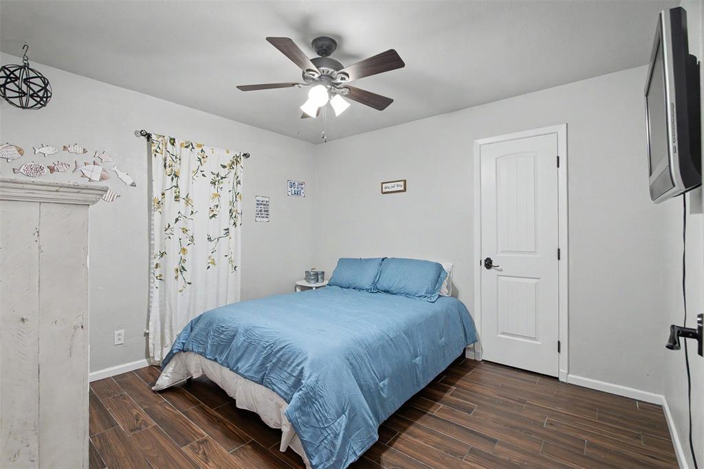 Interior space featuring wood-finish flooring, a multi-blade ceiling fan with integrated lighting, and a solid-core interior door with a matte black lever handle