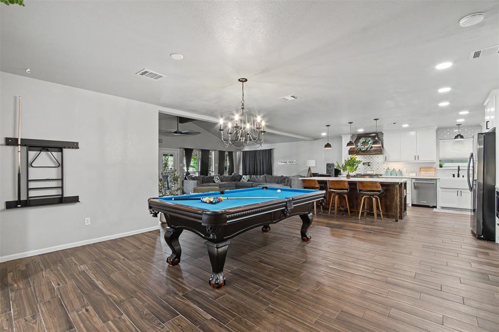 Open-concept area featuring wood-finish flooring, recessed lighting, a decorative chandelier, and a kitchen equipped with white cabinetry, a center island with a wood base, and a farmhouse-style sink