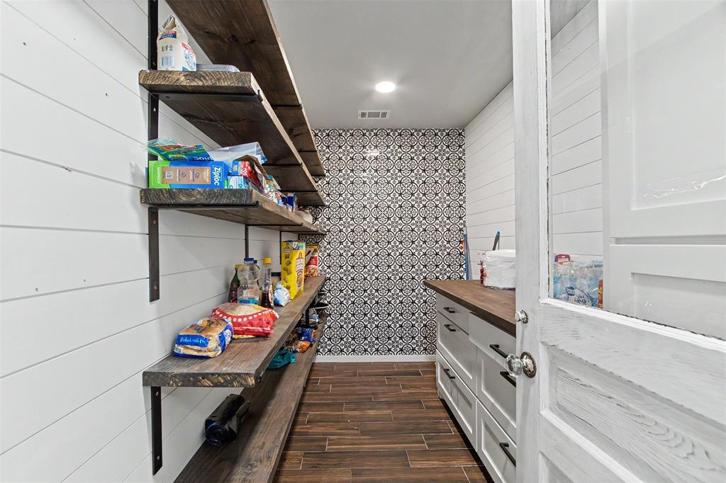 Walk-in pantry featuring open wood-finish shelving, shiplap wall paneling, patterned tile accent wall, wood-finish flooring, and white cabinetry with dark hardware
