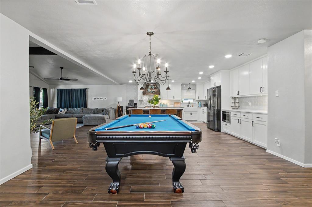 Open-concept interior featuring wood-finish flooring, a multi-arm iron chandelier, recessed lighting, and kitchen cabinetry with integrated appliances