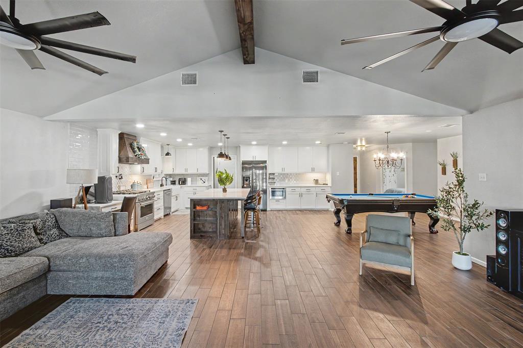 Vaulted ceilings with exposed timber beam, wood-finish flooring, central kitchen island with wood base, white cabinetry, and dual ceiling fans