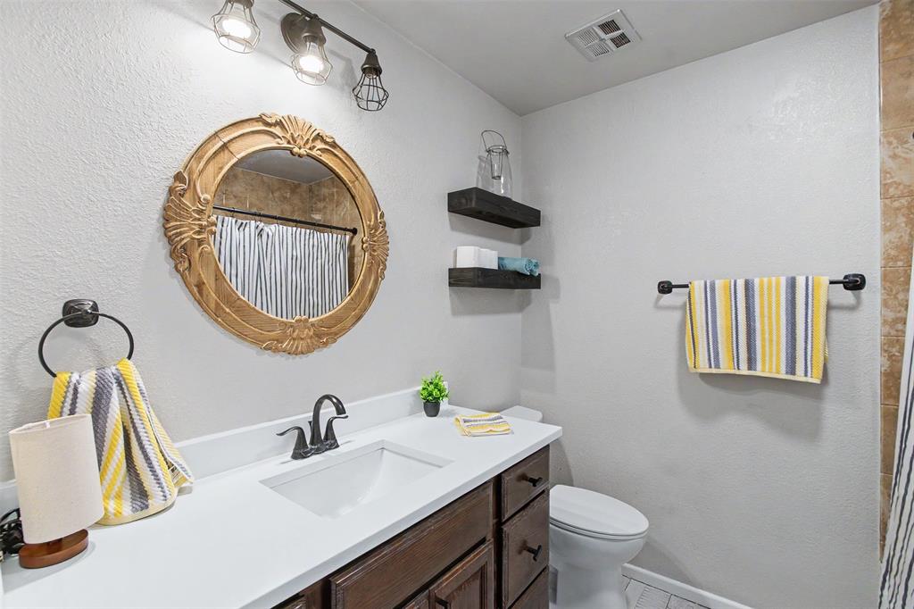 Bathroom featuring a vanity with white countertop, dark wood-finish cabinetry, matte black hardware, and a circular decorative mirror with ornate detailing