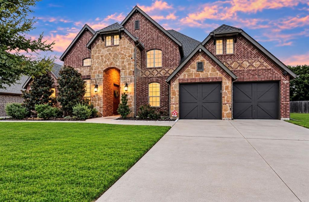 Multi-gabled brick and stone exterior featuring a concrete driveway, two-car garage with cross-buck detailing, and arched windows Multi-gabled brick and stone exterior featuring a concrete driveway, two-car garage with cross-buck detailing, and arched windows
