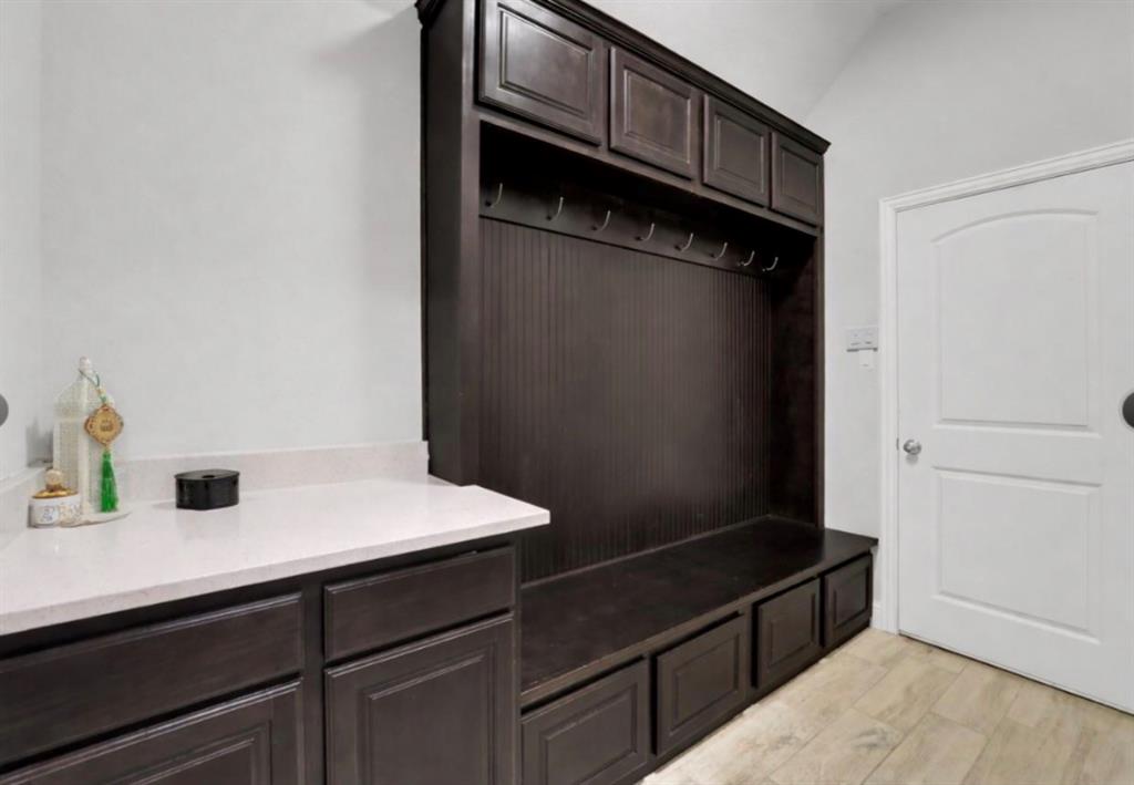 Built-in dark wood cabinetry featuring integrated storage bench, beadboard detailing, and overhead lockers, complemented by a stone-surface countertop and wood-finish flooring