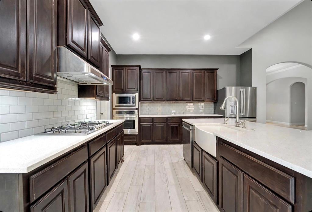 Kitchen featuring dark-finish cabinetry, stone-surface countertops, white subway tile backsplash, farmhouse sink, and wood-finish tile flooring