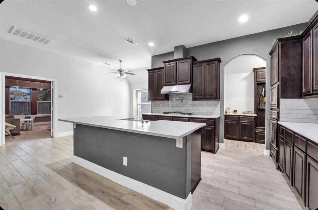 Kitchen featuring a central island with quartz countertops, custom wood cabinetry, a subway tile backsplash, built-in stainless steel oven, and wood-finish tile flooring