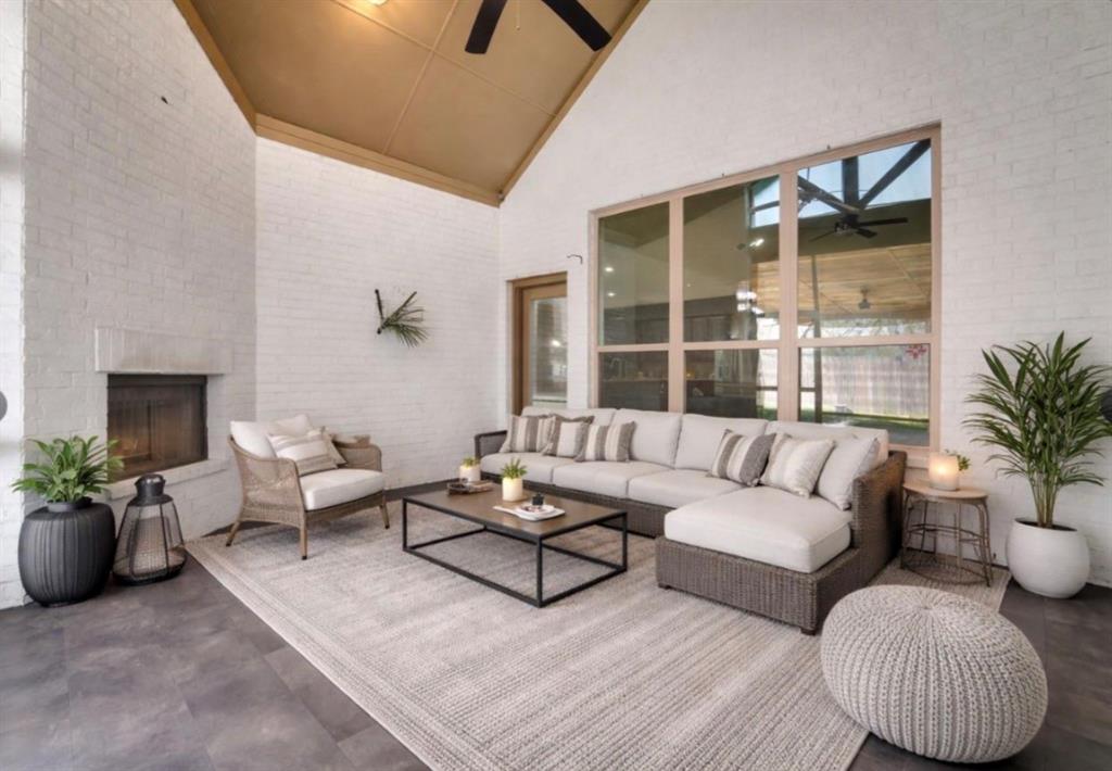 Covered patio featuring white brick walls, vaulted ceiling, large multi-pane windows, and a built-in fireplace