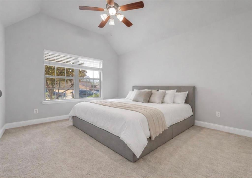 Vaulted ceiling with a centrally mounted ceiling fan, neutral wall tones, carpeted flooring, and a large multi-pane window