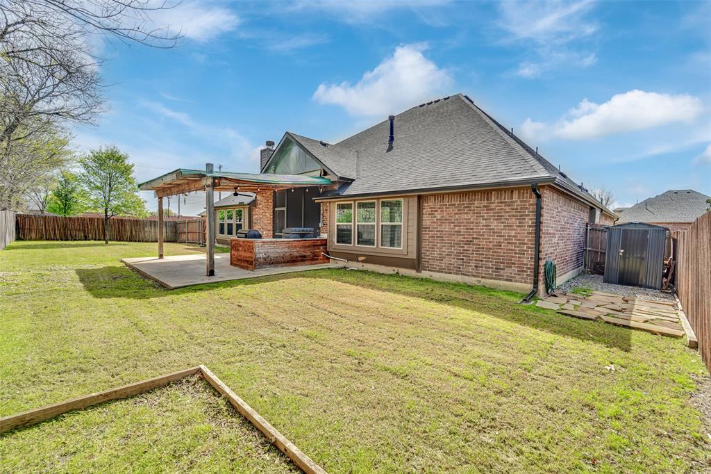 Rear exterior featuring a brick facade, covered wood-beam patio, concrete slab, and wood privacy fencing