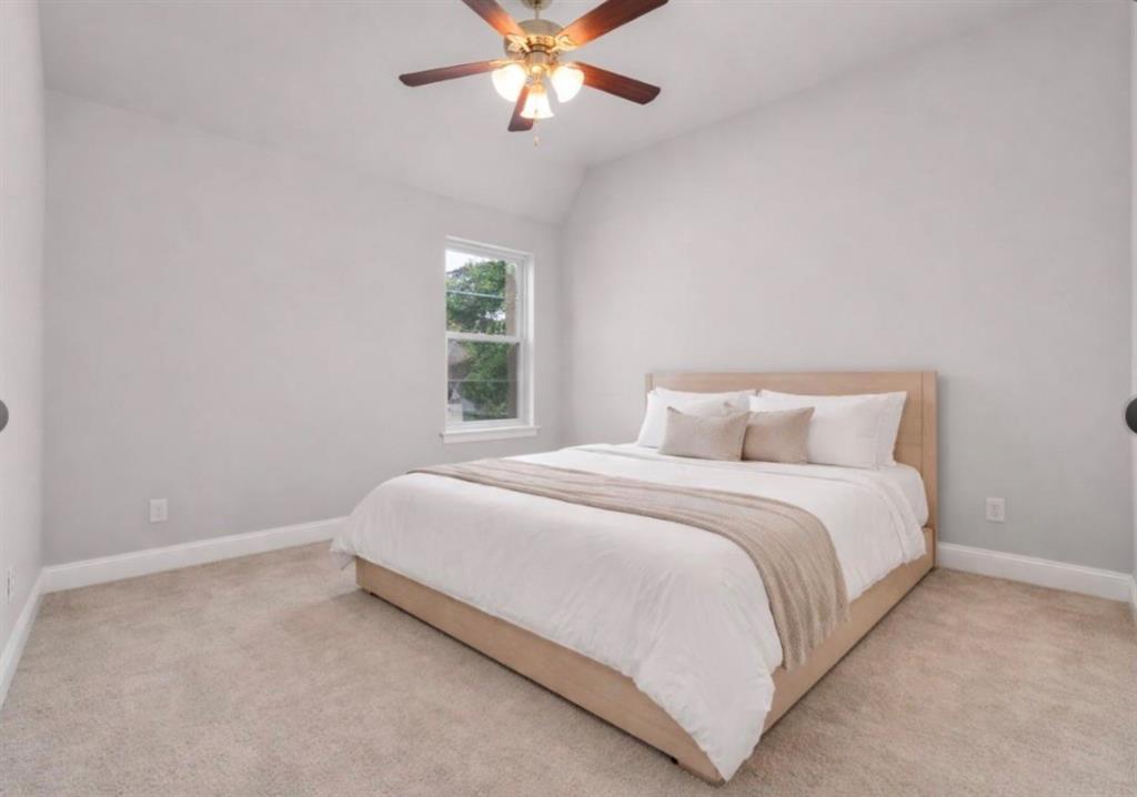 Vaulted ceiling, neutral wall tones, plush wall-to-wall carpeting, single-pane window, and a multi-blade ceiling fan with integrated light fixture