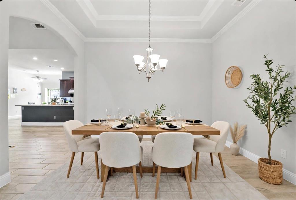 Dining area featuring a tray ceiling, arched entryway, and multi-arm chandelier
