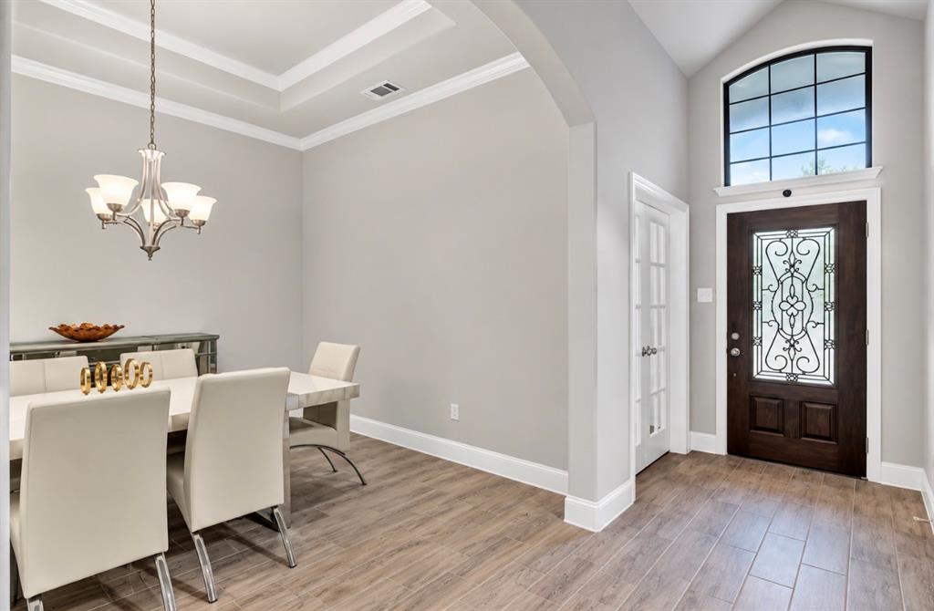 Entryway featuring a wood-finish entry door with decorative iron inlay, arched transom window, wood-finish flooring, tray ceiling, and multi-arm chandelier