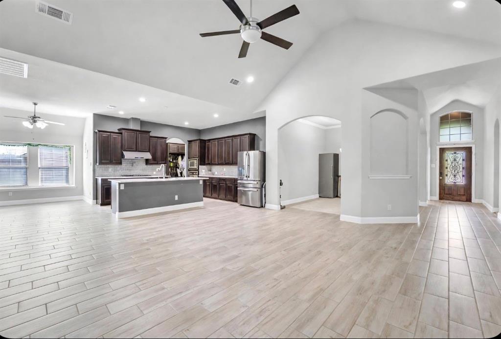 Open-concept interior featuring vaulted ceilings, wood-finish flooring, dark cabinetry, recessed lighting, and an arched entryway with decorative transom window