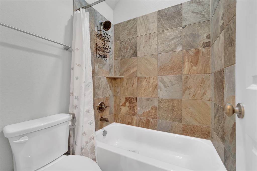 Full-size bathtub with multi-toned stone tile surround, integrated shelving, and bronze-finish plumbing fixtures