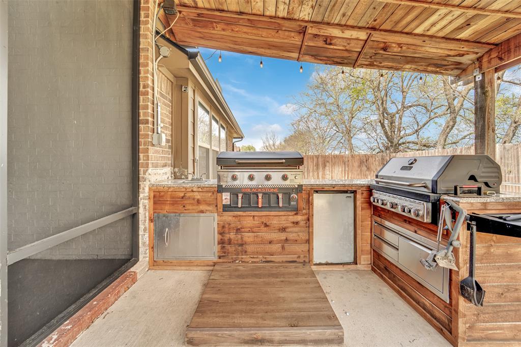 Covered outdoor kitchen featuring wood-paneled cabinetry, stone countertops, stainless steel appliances, and a wood-slat ceiling