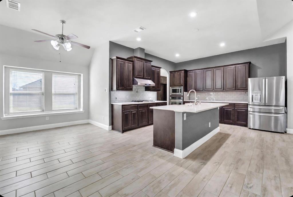 Kitchen featuring dark wood cabinetry, a central island with a stone countertop, stainless steel appliances, subway tile backsplash, and wood-finish tile flooring