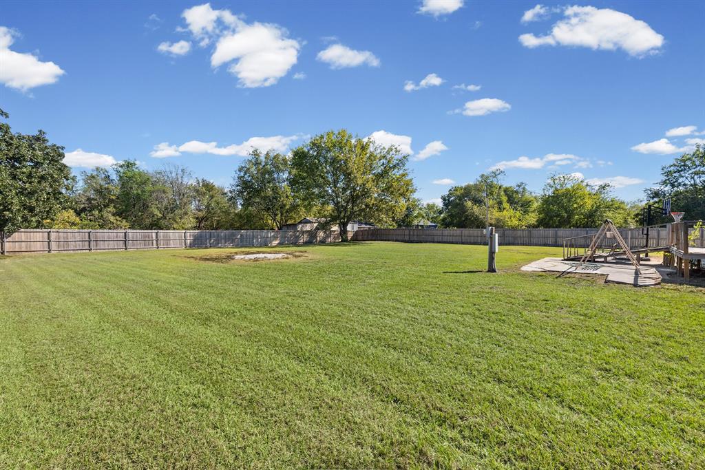 Expansive backyard featuring a large grass lawn, perimeter wood fencing, and mature trees