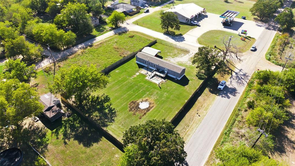 Aerial perspective of a property featuring a fenced perimeter, expansive lawn, detached storage structure, and a covered carport Aerial perspective of a property featuring a fenced perimeter, expansive lawn, detached storage structure, and a covered carport