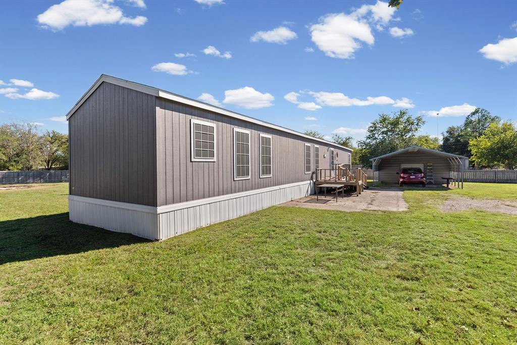 Exterior featuring vertical siding, grid-pattern windows, wood-deck entrance, and a detached metal carport on a fenced lot