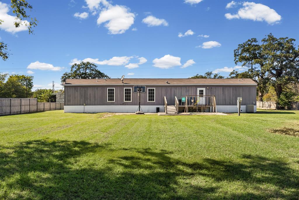 Exterior elevation featuring vertical siding, a raised wooden deck with railings, and a spacious rear lawn enclosed by a perimeter fence Exterior elevation featuring vertical siding, a raised wooden deck with railings, and a spacious rear lawn enclosed by a perimeter fence