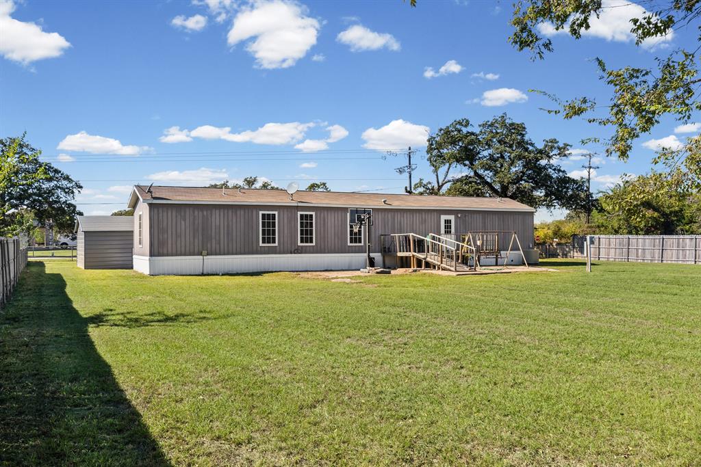 Expansive backyard featuring a large grass lawn, a detached storage shed, wood decking with handrails, and perimeter fencing