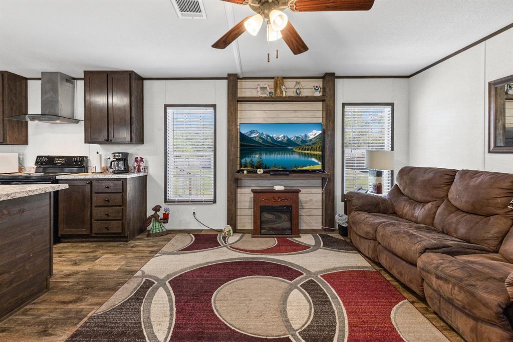 Dark wood cabinetry, wood-finish flooring, built-in entertainment center with shiplap accent, and ceiling fan with light fixture Dark wood cabinetry, wood-finish flooring, built-in entertainment center with shiplap accent, and ceiling fan with light fixture