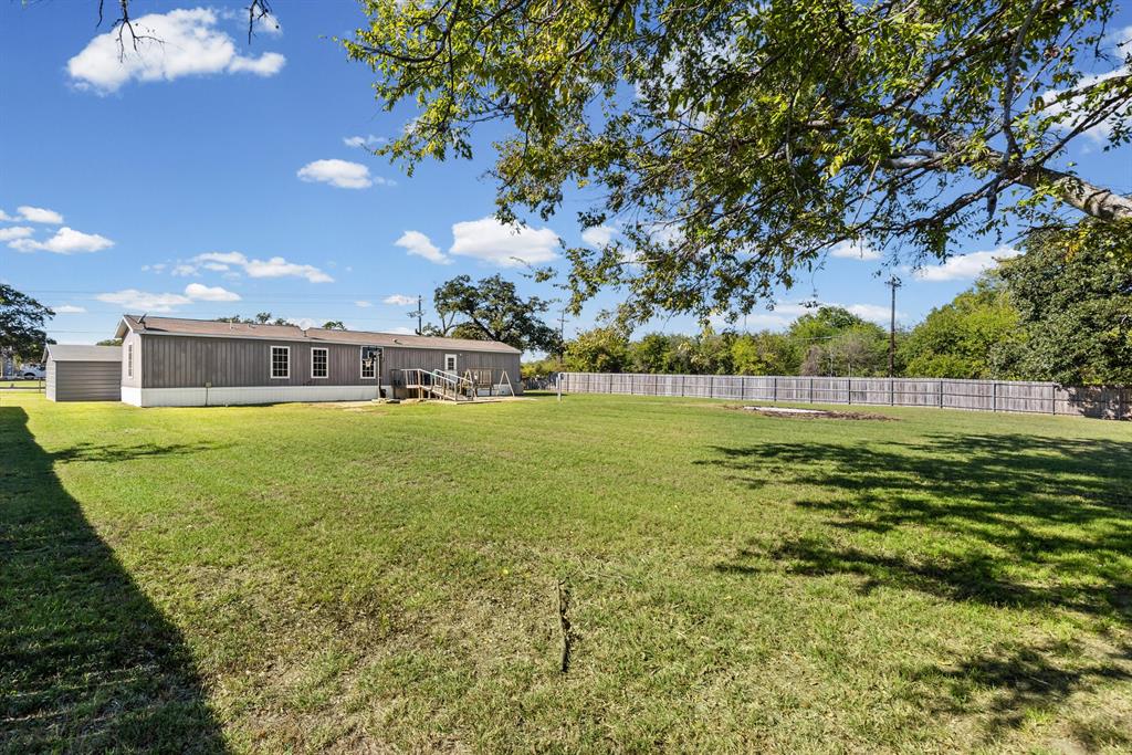 Expansive backyard featuring a level lawn, mature trees, and perimeter wood fencing