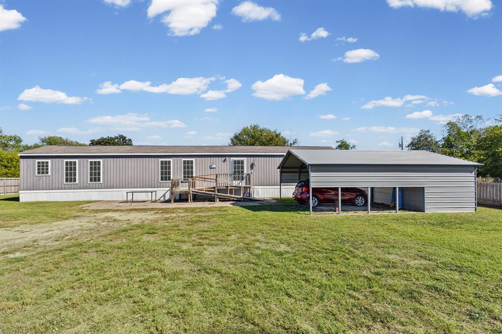 Exterior featuring vertical siding, a metal-roofed carport, a wooden accessibility ramp, and a sprawling lawn Exterior featuring vertical siding, a metal-roofed carport, a wooden accessibility ramp, and a sprawling lawn
