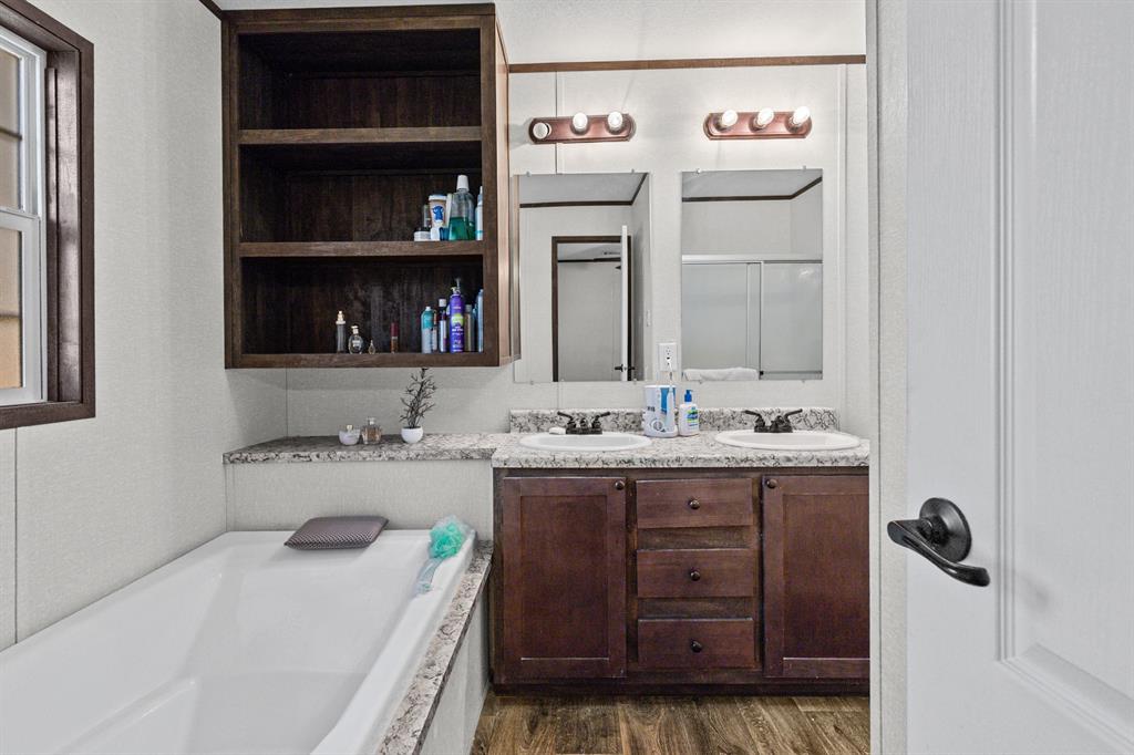 Bathroom featuring a dual-sink vanity with dark wood-finish cabinetry, a built-in open shelving unit, stone-patterned countertops, and wood-finish flooring