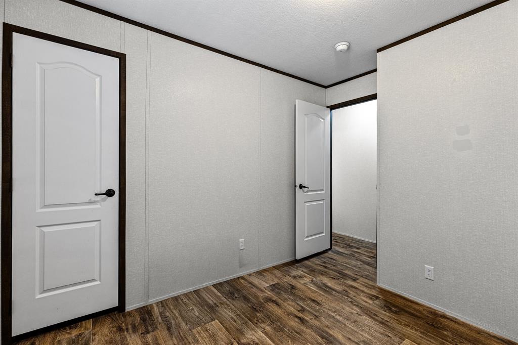 Bedroom space featuring textured wall panels, wood-finish flooring, and white two-panel interior doors with dark hardware and matching trim