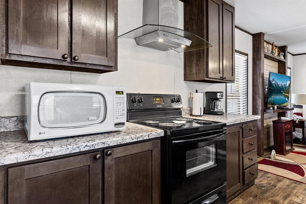 Kitchen featuring stained wood cabinetry, stone-pattern laminate countertops, electric range, glass-panel range hood, and wood-finish flooring