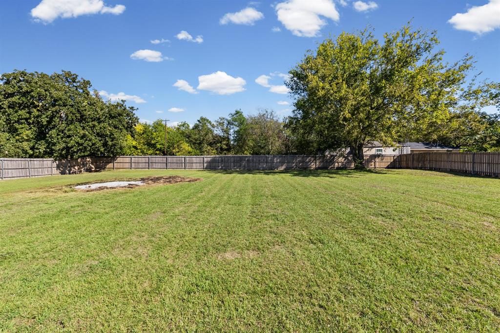 Expansive backyard featuring a large grass lawn, perimeter wood fencing, and mature trees