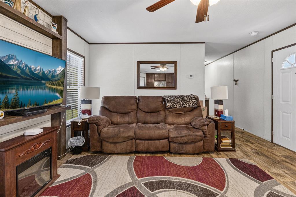 Living area featuring wood-finish flooring, a ceiling fan with integrated lighting, and a built-in entertainment center with a fireplace insert Living area featuring wood-finish flooring, a ceiling fan with integrated lighting, and a built-in entertainment center with a fireplace insert