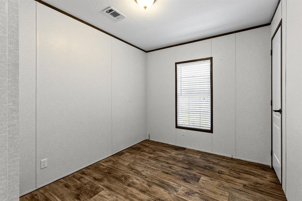 Bedroom featuring wood-finish flooring, a single-window configuration with horizontal blinds, neutral panel walls, dark trim, and a ceiling-mounted light fixture