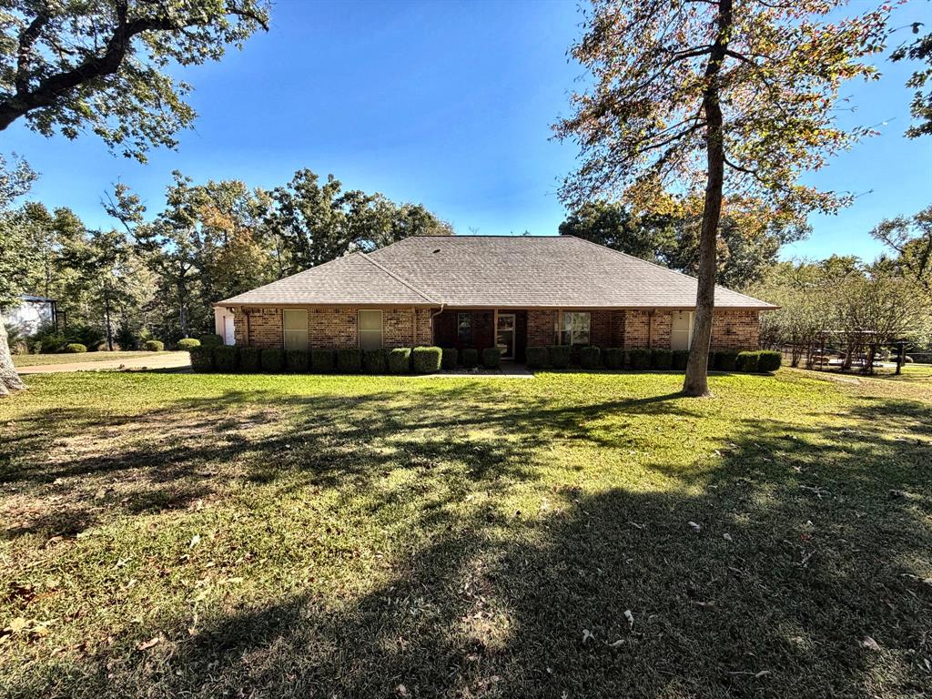 Single-story brick exterior featuring a hip roof, large front yard, and mature canopy trees