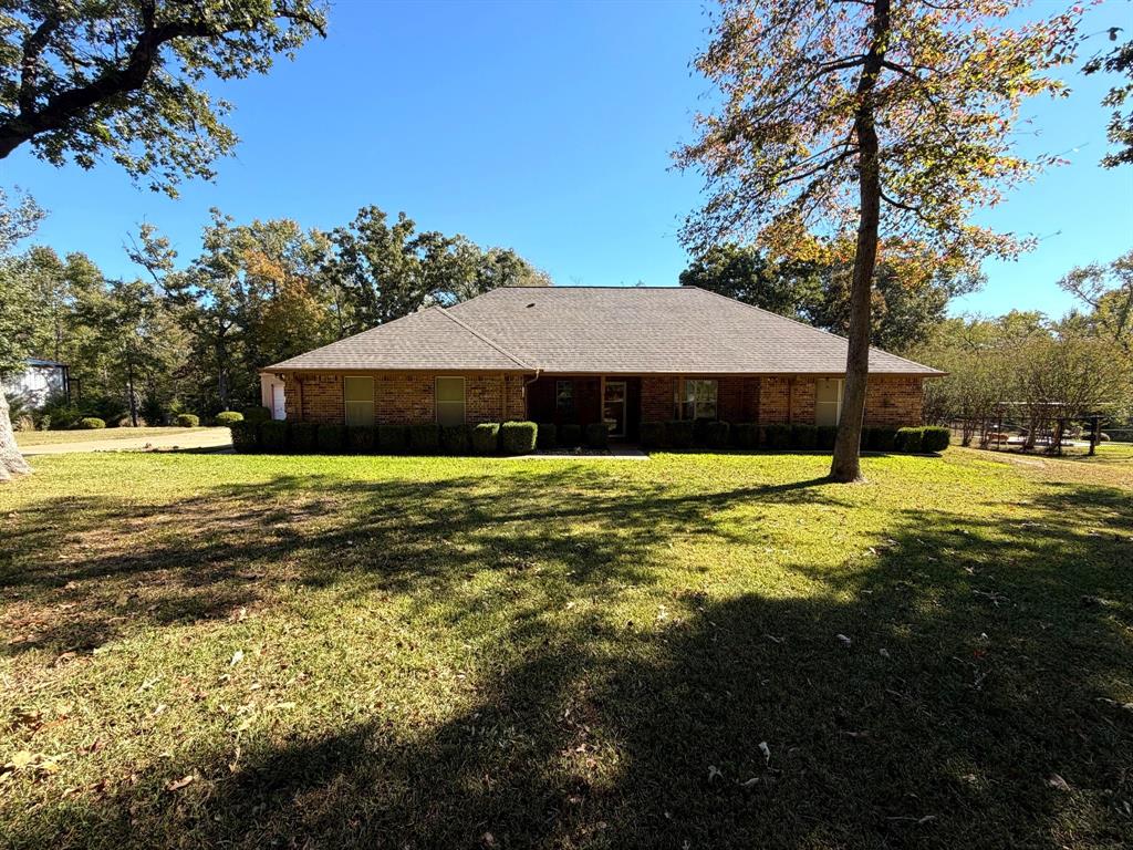 Single-story brick exterior featuring a hipped roof, covered entryway, and mature trees situated on a spacious lot