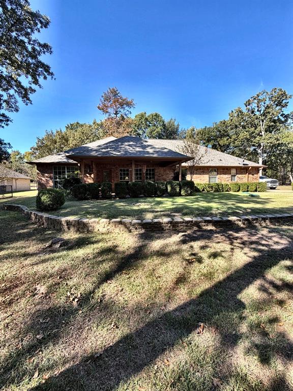 Brick exterior residence featuring a covered front porch, stone retaining wall, and mature trees on the surrounding lot