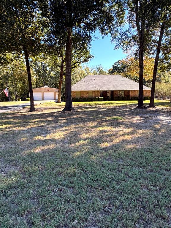 Brick exterior residence featuring a hip roof, multi-car detached garage, and mature trees situated on a spacious lot