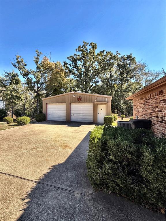 Detached two-car garage featuring metal siding, dual roll-up doors, a side-entry door, and an expansive concrete driveway