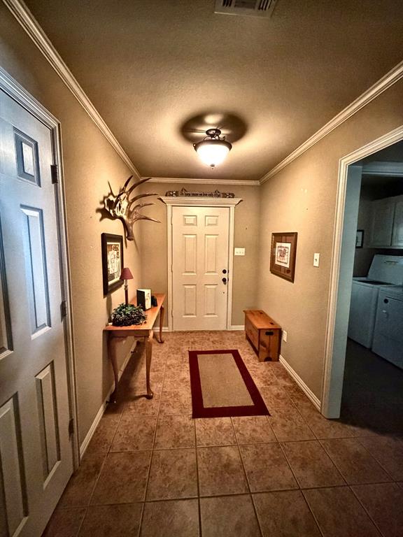 Entryway featuring six-panel door with architectural molding, neutral tile flooring, crown molding, and semi-flush mount dome lighting