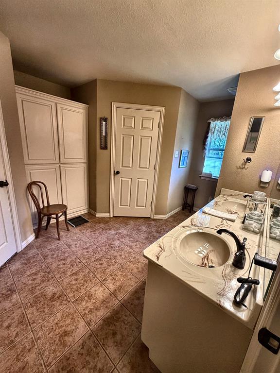 Bathroom featuring dual-sink vanity with patterned stone-finish countertop, tile flooring, built-in floor-to-ceiling storage cabinetry, and multi-light vanity fixture