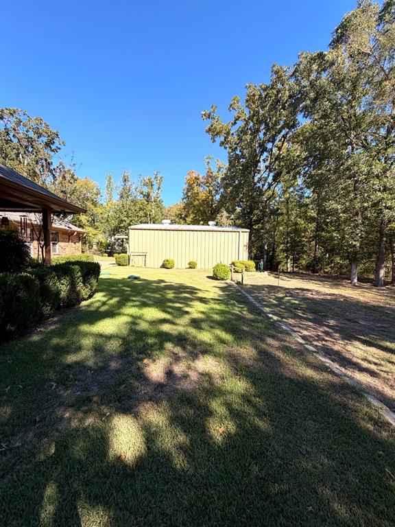 Expansive backyard featuring a metal detached structure, manicured grass, mature trees, and tiered landscaping