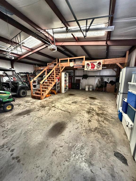 Spacious workshop featuring a concrete floor, exposed steel beams, translucent roof panels, and an elevated wooden loft with a built-in staircase