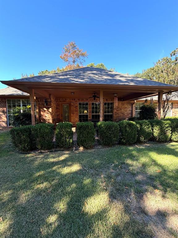 Brick exterior featuring a covered patio, hipped roofline, multiple windows, and a manicured lawn