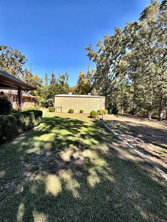 Expansive backyard featuring a metal detached structure, mature trees, and landscaping