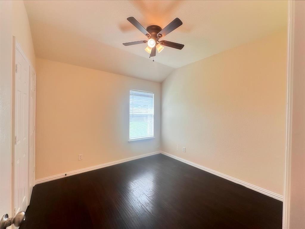Empty room featuring ceiling fan, vaulted ceiling, and dark wood-type flooring