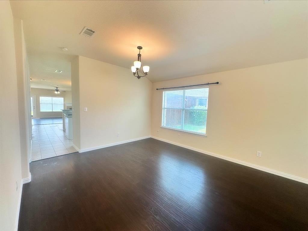 Spare room featuring ceiling fan with notable chandelier, plenty of natural light, and dark hardwood / wood-style flooring